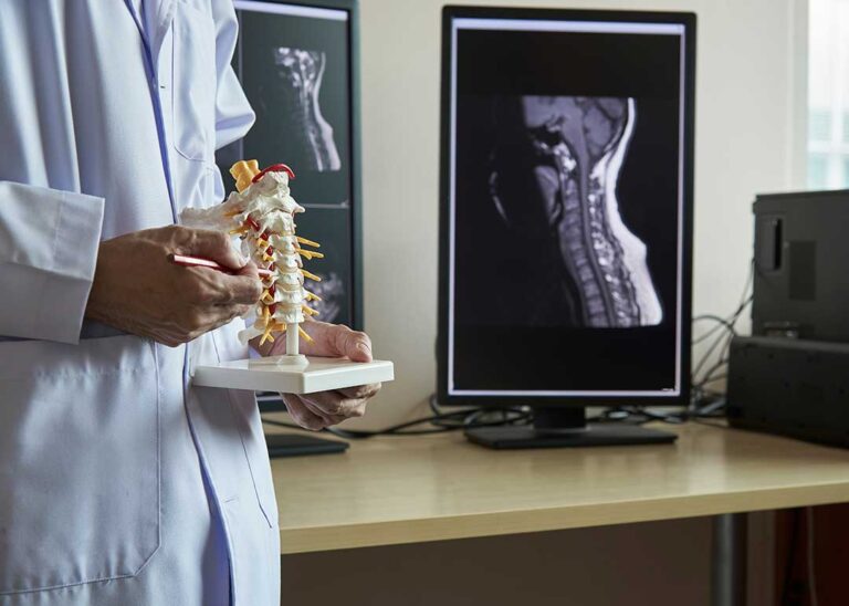 Person sitting at a table holding their wrist, showing discomfort while using a laptop.
