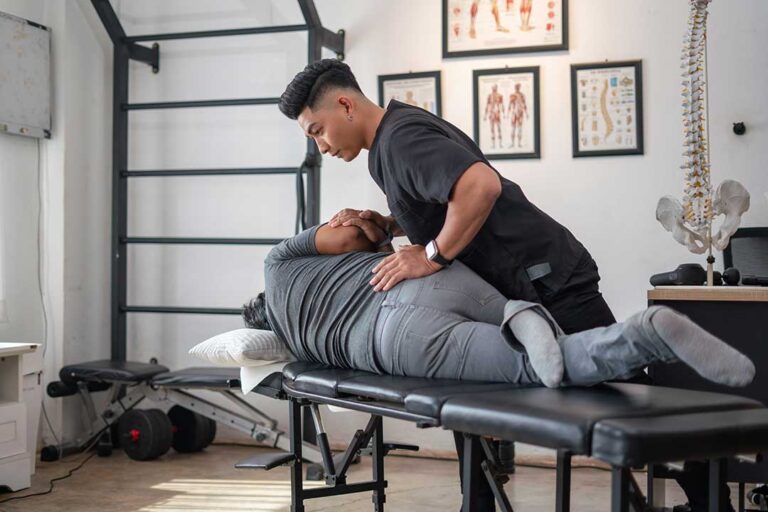 Adult practicing back mobility exercises beside a treatment table in a bright clinic room.